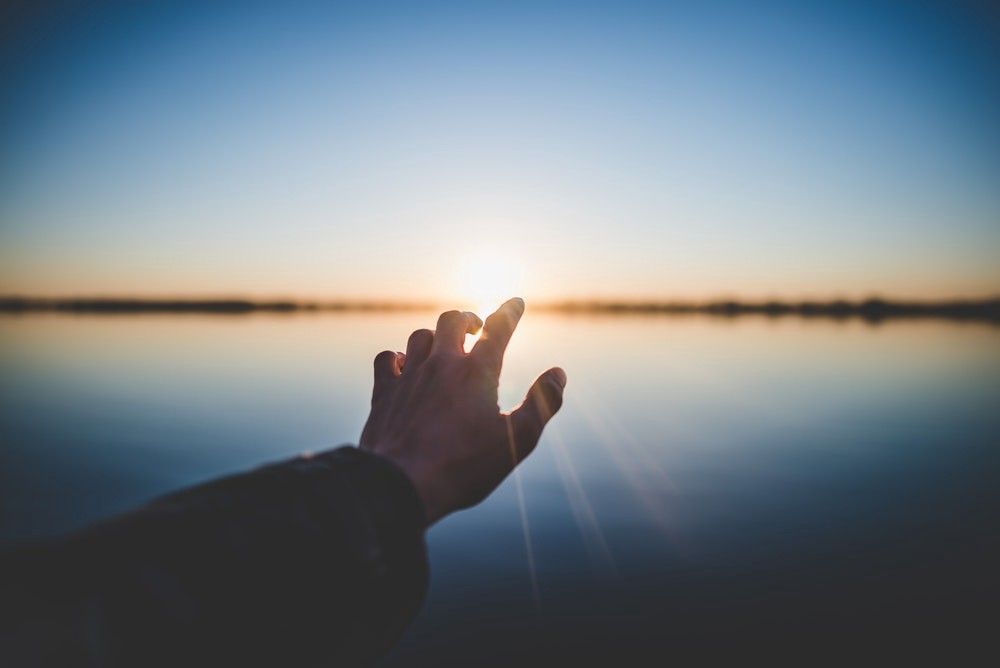 a hand pointing towards sun on the other side ocean