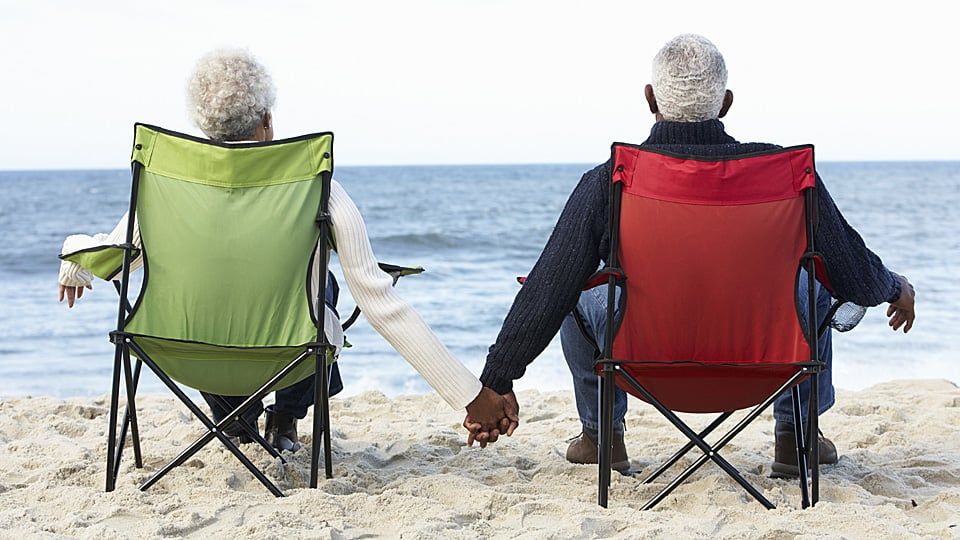 an old couple sitting on the beach holding hands