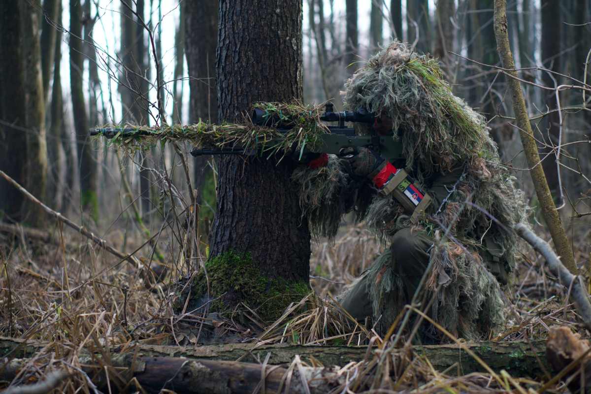 A Person In Camouflage Holding A Gun In The Forest